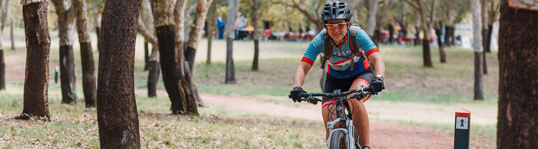 a cyclist riding through the cork oak forest with event tents visible in the distance