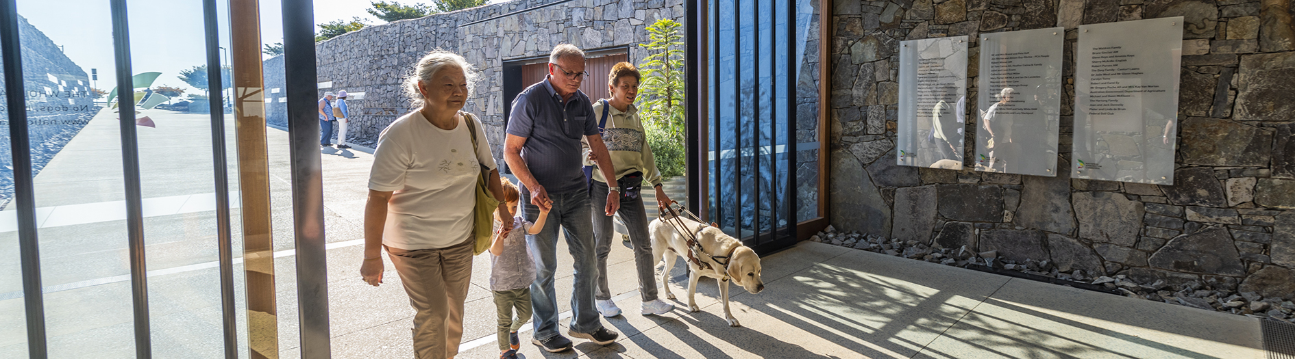 photo of family entering the arboretum visitors centre, accompanied by a companion dog