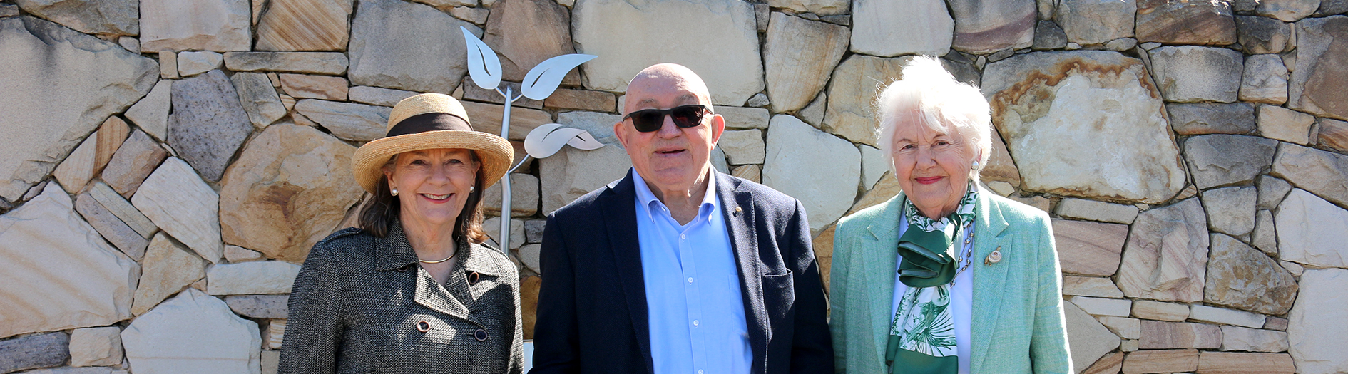 3 adults stand in front of a stone garden wall: L-R Helen Stevens, John Mackay and Tamie Fraser (AO)