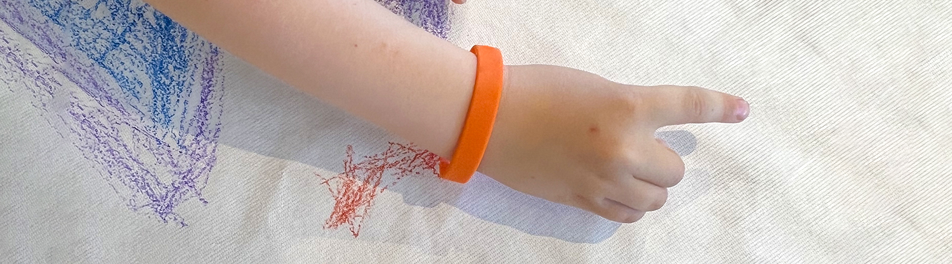 small childs hand with orange wrist band draws on a kite surface