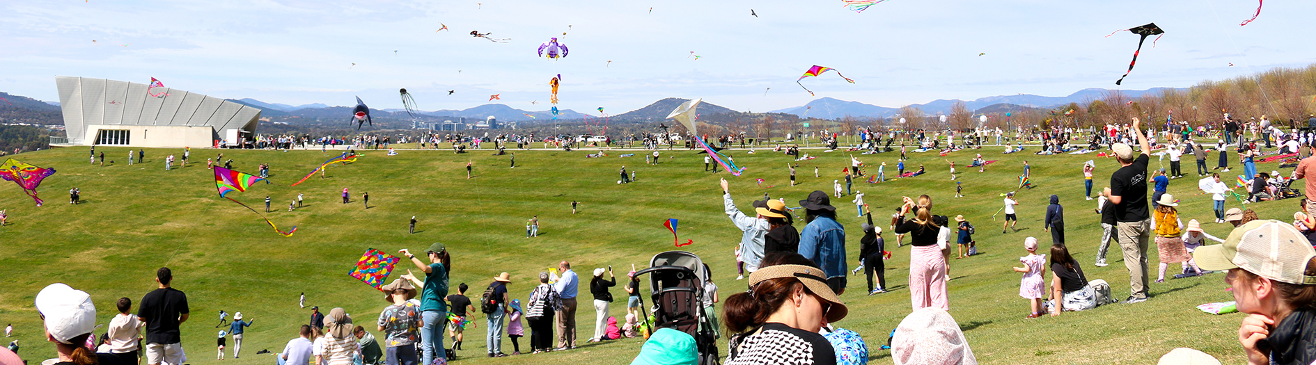 Crowds fill the top of the amphitheatre filling the skies with kites on a sunny day
