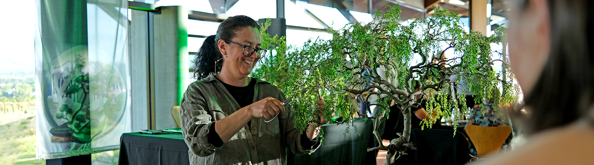Female bonsai artists smiling as she demonstrates pruning a bonsai
