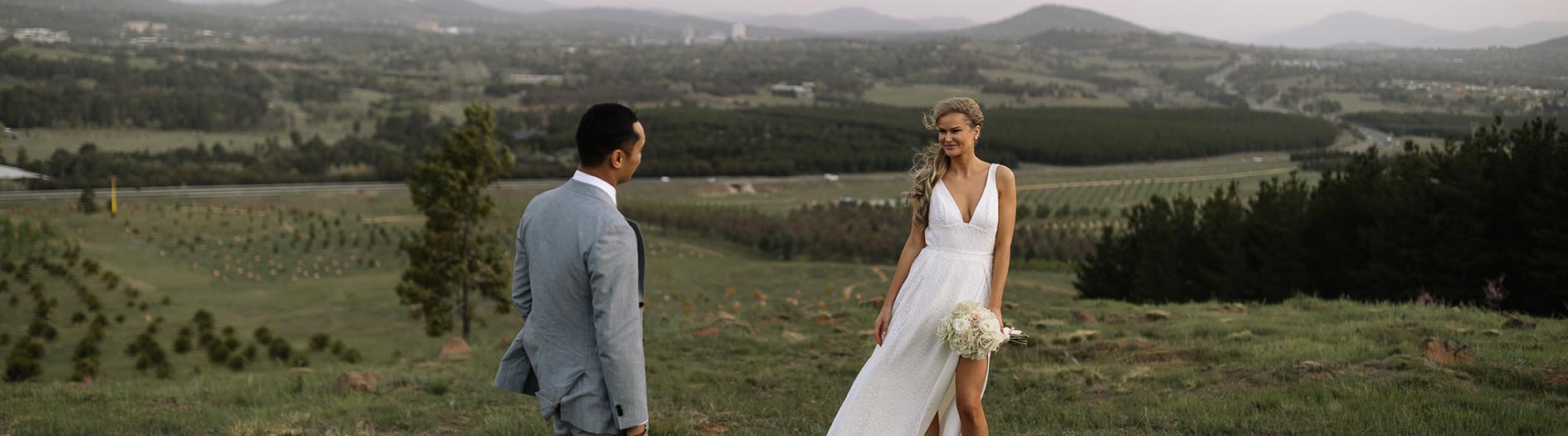 a bride and groom standing at the hilltop lookout with the arboretum forests in the background