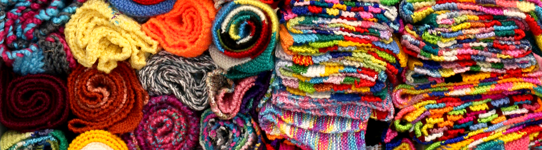 Rolled and folded brightly coloured Warm Trees Scarves stacked high