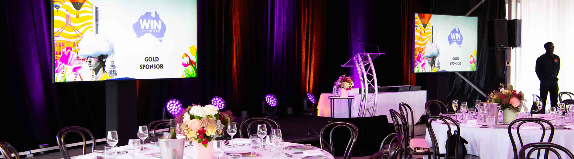Photo of the table setting at the awards night with screens showing the award sponsors in the backgound