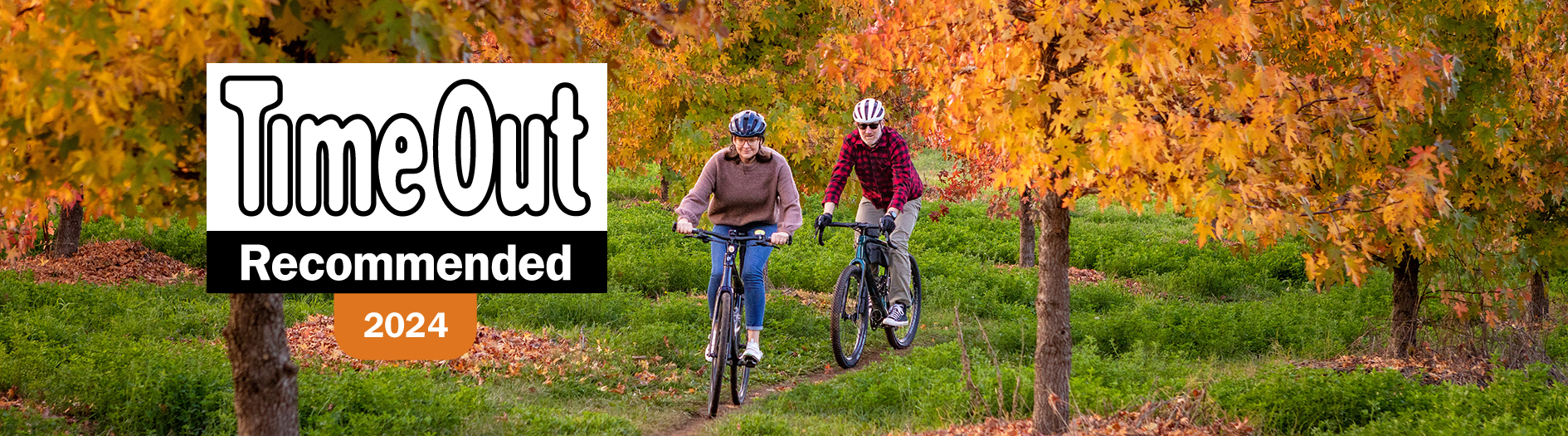 Image of 2 people riding through a forest on bikes among the autumn colour, a logo appears on the left which reads 'TimeOut, Recommended, 2024'.