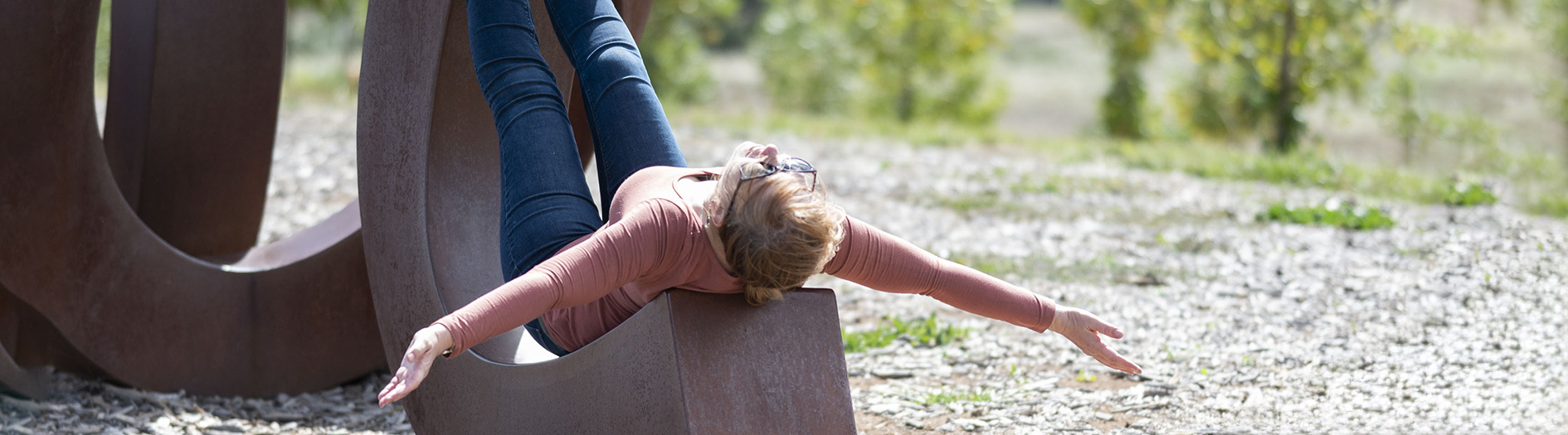 a blonde women lays back on the curves of the large metalic 'wide brown land' sculpture, resting in the sun