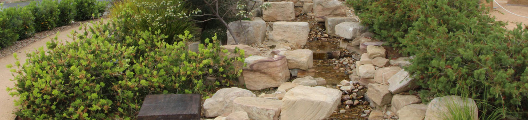 A man-made creek lined with pale orange sandstone rock and low green shrubs