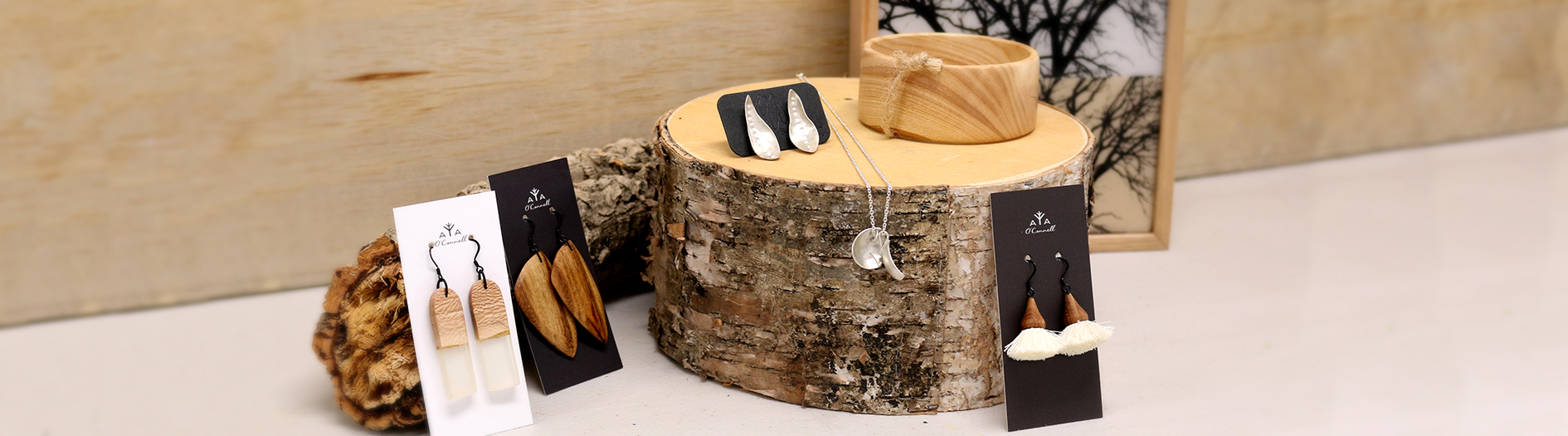 Selection of earrings and a necklace from The Curatoreum displayed on logs in front of a wooden background.