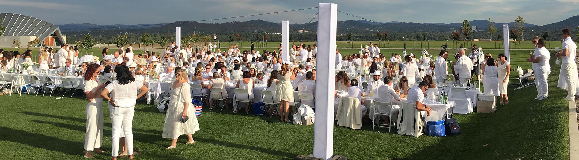 outdoor dining event with people and long tables elegantly dressed in all white