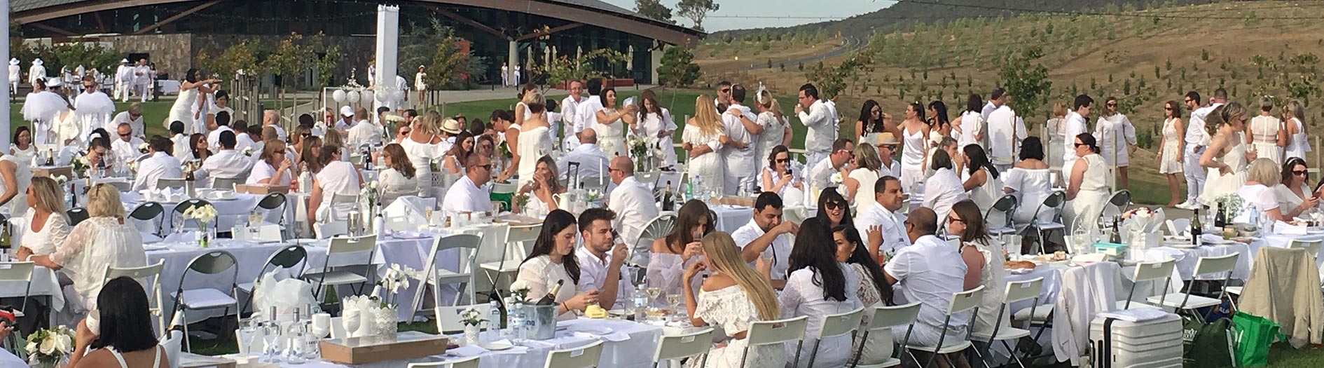 outdoor dining event with people and long tables elegantly dressed in all white