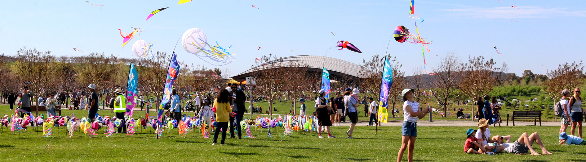 Crowds of families fly colourful kites on the grassy events terrace on a sunny day